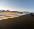 Reynisfjara black sand beach at sunset illuminated by the last rays of the sun from the horizon of the sea with tourists amazed