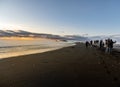 Reynisfjara black sand beach at sunset illuminated by the last rays of the sun from the horizon of the sea with tourists amazed