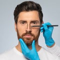 Rhinoplasty concept. Handsome middle aged man with marking on his nose standing on grey background, closeup, cropped