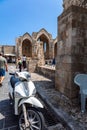 Narrow cobbled historical streets of Rhodes. Tourists walk on Old Town. Vintage scooter bike is parked old stone against