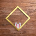 Rhomboid gold frame and bunny white pink ears on a wooden background. Text space. Top view. Minimal style