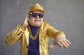 Funny senior man in golden jacket, baseball cap and chain necklace playing music at disco party