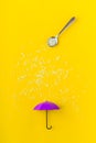 Rice grains pouring from spoon on purple toy umbrella on yellow background. Artistic concept of spring rain Royalty Free Stock Photo