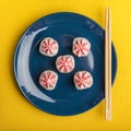 Rice rolls with pink Lava sauce, on a dark blue plate with bamboo sticks. Yellow background. Minimalist style