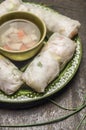 Rice rolls with vegetables and chicken on a green plate with vegetable soup on wooden rustic background close up