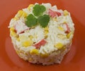 Rice salad with crabs corn with mayonnaise dressing, served on an orange plate and decorated with greens. Elegant salad serving