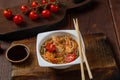 Rice with shrimp in Thai yakisoba style on a wooden stand next to cherry tomatoes, soy sauce and chopsticks