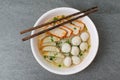 Rice stick noodles in broth with pork and meatballs in bowl on tile table