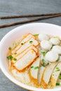 Rice stick noodles in broth with pork and meatballs in bowl on tile table