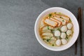 Rice stick noodles in broth with pork and meatballs in bowl on tile table