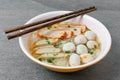 Rice stick noodles in broth with pork and meatballs in bowl on tile table