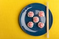 Rice sushi roll with pink Lava sauce, on a dark blue plate with bamboo sticks with space for text. Yellow background
