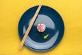 Rice sushi roll with pink Lava sauce and wasabi, on a dark blue plate with bamboo sticks. Yellow background