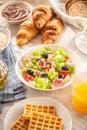 Rich breakfast assortment with salad, croissants, waffles, bread and orange juice