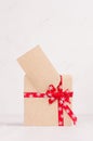 Rich bright gift box of kraft paper with red ribbon and blank greeting card closeup on white wood table.