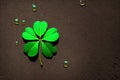 A brown surface is adorned with water droplets, and amidst them lies a four-leaf clover.