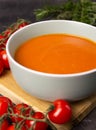 Rich color tomato puree soup in a gray bowl on a wooden board with cherry tomatoes and herbs on a background Royalty Free Stock Photo