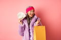 Rich and fashionable asian senior woman wasting money in shops, holding shopping bag and dollars, winking happy at Royalty Free Stock Photo