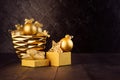 Rich golden Christmas background with golden decoration -  balls in glossy bowl, star, gift box with ribbons on dark wall, wood. Royalty Free Stock Photo