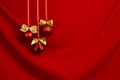 Rich red christmas background - shimmer balls with golden bows hang on ribbons in row on saturated silky wavy backdrop, copy space