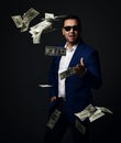 Rich self-confident businessman in blue jacket and sunglasses stands and wastes money, throwing dollars cash at camera