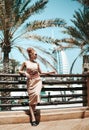Rich stylish gorgeous tourist woman in summer dress is posing on background of famous Dubai skyscrapers during vacation Royalty Free Stock Photo