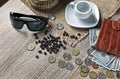 Red wallet with american dollars, various foreign coins and cup of coffee on the table