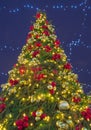 Richly decorated Christmas tree with colorful lights and sparkling balloons at night, outdoors, against a dark blue Royalty Free Stock Photo