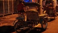 A rickshaw with its driver is waiting for customers on the side of the road at night.