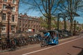 Rickshaw riding on street beside canal and old buildings in sunny day at Amsterdam. Royalty Free Stock Photo