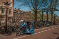 Rickshaw riding on street beside canal and old buildings in sunny day at Amsterdam. Royalty Free Stock Photo