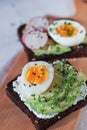 Ricotta and avocado toast with soft boiled egg, microgreen of garden cress and sesame mix on wooden board on white