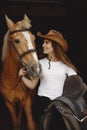 Portrait of rider woman in a leather hat with a brown horse in a stable Royalty Free Stock Photo