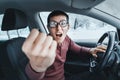 Ridiculous nerd driver in eyeglasses shouting to the camera and showing his fist inside a car. Concept of a newbie