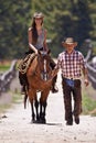 Riding 101. An attractive young cowgirl riding a horse on a ranch while a cowboy walks alongside. Royalty Free Stock Photo