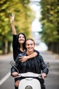 Riding with fun. Beautiful young couple riding scooter together while happy woman raising arms and smiling. Ride and love Royalty Free Stock Photo