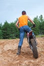 Riding motorcross motorcycle in sandy pit, Caucasian man dressed orange t-shirt standing with bike, rear view