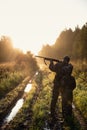 Rifle Hunter and His Son Silhouetted in Beautiful Sunset. Huntsman with a boy and rifle in a forest on a sunrise. Royalty Free Stock Photo