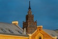 Riga Academy of Sciences tower and old brick rooftops illuminated by warm sunset light showing historical architecture contrast, Royalty Free Stock Photo