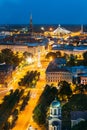 Riga, Latvia. Aerial View Of Cityscape In Evening Night Lights Illumination. Summer Top View Of St. Peter's Church