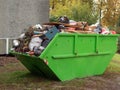 Riga / Latvia 10/07/2019 Big green color metal skip container full of trash by a house building