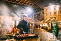 Riga, Latvia. Young Man frying pork - a traditional Christmas dish of street food on streets of Europe in winter during