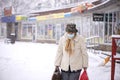 Riga, Latvia, - January 11, 2021: An old sick woman with a protective face mask and a shopping bags in the city during a snowstorm