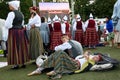 Young woman in traditional Latvian folk dress lying down on the ground and relaxing with smartphone before Dance performance.