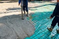 Rigger holding pump hose to pouring fresh concrete, other worker is using hook to pull up square reinforcing steel bars