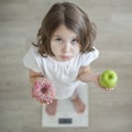 Right choice. Little sad girl holding in hands green apple and highcalorie donut. Kid trying to make decision between healthy Royalty Free Stock Photo