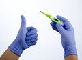 Right hand in blue glove holding a green medical thermometer, left hand thumb up Royalty Free Stock Photo