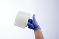 Right hand in blue glove holding with index finger a roll of toilet paper Royalty Free Stock Photo