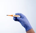 Right hand in blue glove holding a orange medical thermometer Royalty Free Stock Photo