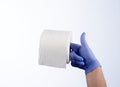 Right hand in blue glove holding with index finger a roll of toilet paper Royalty Free Stock Photo